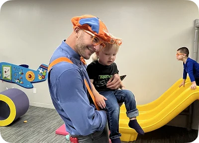 An image of a staff member holding a child near an indoor play slide.